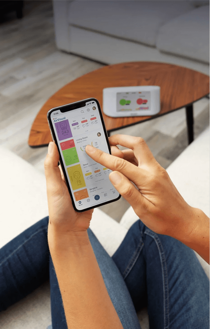 hands on phone with AirVisual App open and AirVisual Pro in background